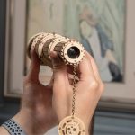 Hand hält ein Holz-Teleskop-Objektiv mit Kette, dekoratives wissenschaftliches Gadget aus Holz, ideal für Wissenschafts- und Dekorationszwecke.