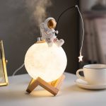 Niedliche Nachtlampe in Form eines Astronauten, der auf einer leuchtenden Mondbasis sitzt, ideal für Kinderzimmer und als dekoratives Science-Gadget.