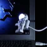 Kleine Astronautenfigur mit leuchtendem Kopf, verbunden mit Kabel, vor dunklem Hintergrund, ideal für Wissenschafts- und Dekorationszwecke.