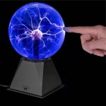 Tesla-Spule mit blauer elektrischer Entladung, die durch Handkontakt aktiviert wird, auf schwarzem Hintergrund.