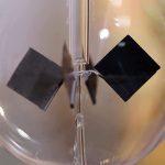 Nahaufnahme einer magnetischen Kristallstruktur in einem transparenten Glas, die schwarze und silberne Kristalle zeigt, die durch Magnetkraft angeordnet sind.