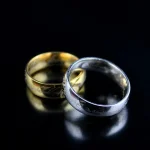 Zwei Eheringe, ein goldener und ein silberner, liegen auf einer schwarzen Oberfläche, symbolisieren Liebe und Verbundenheit.