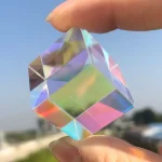 Hochwertiger, transparenter Kristallwürfel mit Regenbogeneffekten, gehalten zwischen Daumen und Zeigefinger. Perfekt für wissenschaftliche Dekorationen und Sammlerstücke.