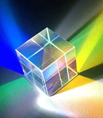 Transparenter Kristallwürfel, der Licht in Regenbogenfarben bricht, auf einer bunten Oberfläche.