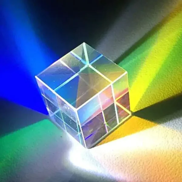Transparenter Kristallwürfel, der Licht in Regenbogenfarben bricht, auf einer bunten Oberfläche.