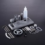 Präziser physikalischer Experimentieraufbau mit verschiedenen Metallteilen, Schrauben, Gummibändern und einem Fläschchen auf schwarzem Hintergrund.