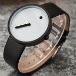 Modernes minimalistisches Armbanduhr-Design mit weißem Zifferblatt, schwarzem Zeiger und kleinem schwarzen Punkt, auf schwarzem Lederarmband.