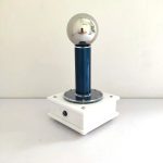 Wissenschaftliches Experimentiergerät mit metallischer Kugel auf blauer Säule, auf weißem Basis, ideal für physikalische Demonstrationen.