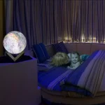 Leuchtende Sphäre auf Nachttisch neben Kind im Bett, schafft eine magische Atmosphäre im Schlafzimmer.