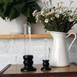 Elegante Kerzenhalter aus transparentem Glas mit schwarzem Holzsockel, ideal für stilvolle Dekorationen und wissenschaftliche Präsentationen.