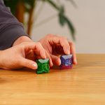 Zwei bunte, glitzernde Stein-Modelle, die von einer Person auf einem Holztisch gehalten werden, symbolisieren wissenschaftliche Experimente und Dekoration.