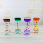 Farbige Sanduhren aus Glas in verschiedenen Farben, transparentes Design, auf weißem Holzuntergrund, ideal für Dekoration und wissenschaftliche Präsentationen.