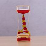 Transparentes Glas mit rot-gelben Kugeln, die in einer vertikalen Anordnung angeordnet sind, auf einem neutralen Hintergrund.