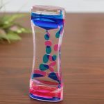 Transparentes Glas mit farbiger, schichtweise angeordneter Flüssigkeit in Blau, Pink und transparentem Bereich, zeigt wissenschaftliches Experiment.