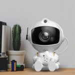 Niedlicher Kameraroboter mit Sternen-Design, ideal für Kinderzimmer oder als Dekoration, ausgestattet mit Kamera und LED-Licht, auf einem Holzschreibtisch neben Pflanzen.