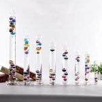 Verschiedene große und kleine Schneekugeln mit bunten Glaskugeln in transparenten Glasbehältern, dekorativ auf einer weißen Oberfläche.