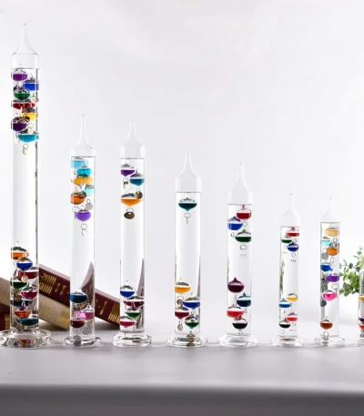 Verschiedene große und kleine Schneekugeln mit bunten Glaskugeln in transparenten Glasbehältern, dekorativ auf einer weißen Oberfläche.