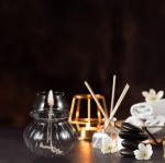 Eleganter Lichtspender in einem transparenten Glas, umgeben von schwarzen Steinen, weißen Blumen und einem warmen Kerzenlicht, ideal für entspannte Raumdekorationen.