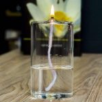 Kerze in einem Glas Wasser, das als Feuerzeug dient, mit Flamme an der Spitze, auf Holztisch.