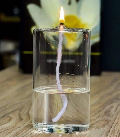 Kerze in einem Glas Wasser, das als Feuerzeug dient, mit Flamme an der Spitze, auf Holztisch.