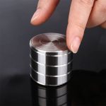 Kleiner, runder Metallwürfel mit glänzender Oberfläche, der von einer Person berührt wird, zeigt die magnetischen Eigenschaften des Metalls.