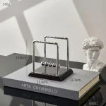 Dekoratives Newtonsches Pendel aus Metall auf einem Buch, ideal für wissenschaftliche Dekorationen und als faszinierendes Lehrmittel.