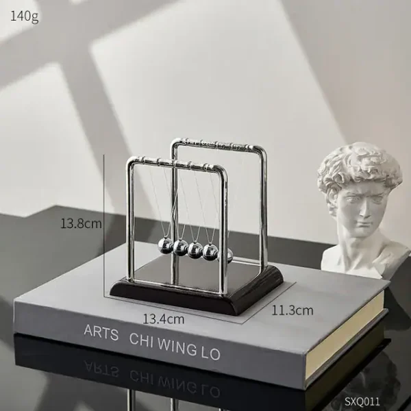 Dekoratives Newtonsches Pendel aus Metall auf einem Buch, ideal für wissenschaftliche Dekorationen und als faszinierendes Lehrmittel.