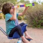 Kleines Kind sitzt im Rollstuhl und schaut durch ein buntes Teleskop, das für Kinder geeignet ist, um den Himmel zu erkunden.