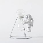 Raumfahrer-Statue neben einer Sanduhr auf einem weißen Hintergrund, dekoratives wissenschaftliches Element.