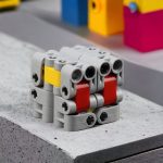Kreativer Roboter aus LEGO-Steinen, gebaut mit bunten Bausteinen in Grau, Rot, Gelb und Blau, auf einer grauen Oberfläche.