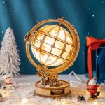 Dekorativer mechanischer Globus mit Weltkarte, beleuchtet, auf winterlichem Hintergrund mit Schneeflocken, Weihnachtsdekoration und Geschenkboxen.