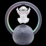 Kleines Raumfahrer-Design mit Astronautenfigur, die auf einem Mond sitzt, umgeben von einem leuchtenden Neon-Ring in Regenbogenfarben, auf schwarzem Hintergrund.