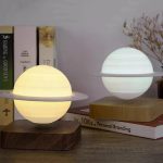 Zwei stilvolle Lampen in Form von Planeten mit Ring, die auf einem Holztablett und einem Bücherstapel auf einem Tisch stehen, ideal für wissenschaftliche Dekoration.
