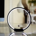 Modernes Lichtdekor mit kreisförmigem LED-Licht und schwebender Glaskugel auf einem weißen Tisch, ideal für stilvolle Raumgestaltung.