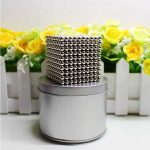 Magnetwürfel mit metallischer Oberfläche auf einer runden Metallbasis, umgeben von gelben Rosen in weißen Pflanzkästen, dekoratives wissenschaftliches Objekt.