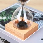Sanduhr mit schwarzem Sand auf Holzsockel, ideal für wissenschaftliches Dekor und moderne Inneneinrichtung, zeigt die Zeit auf elegante Weise.