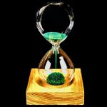 Sanduhr mit grüner Flüssigkeit, die durch die Glaskörper fließt, auf einem Holzsockel, wissenschaftliches Dekorationsstück.