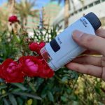 Nahaufnahme eines Mikroskops, das auf rote Blumen gerichtet ist, im Freien mit urbanem Hintergrund. Perfekt für wissenschaftliche und botanische Themen.