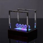 Ein modernes harmonisches Pendel mit leuchtenden Kugeln, das durch LED-Beleuchtung in Blau und Lila beeindruckend wirkt. Perfekt für wissenschaftliche Dekorationen und Experimente.