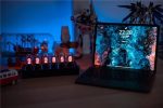 Moderne Nixie-Röhren Uhr neben Laptop auf einem Schreibtisch, umgeben von Dekorationsartikeln und Spielzeug, in einem gut beleuchteten Raum.