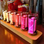 Moderne Nixie-Röhren mit bunten Leuchtanzeigen auf Holzbasis, ideal für Dekoration und Technikliebhaber.