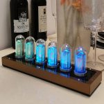 Moderne Nixie-Röhren Uhr mit leuchtenden Zahlen in verschiedenen Blautönen, auf einer eleganten Basis, ideal als stilvolles Dekorationsstück für Technik- und Wissenschaftsliebhaber.