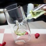 Wissenschaftliches Experiment mit Reagenzglas und gelber Flüssigkeit, das in einem transparenten Becherglas über einem roten und weißen Tisch durchgeführt wird.