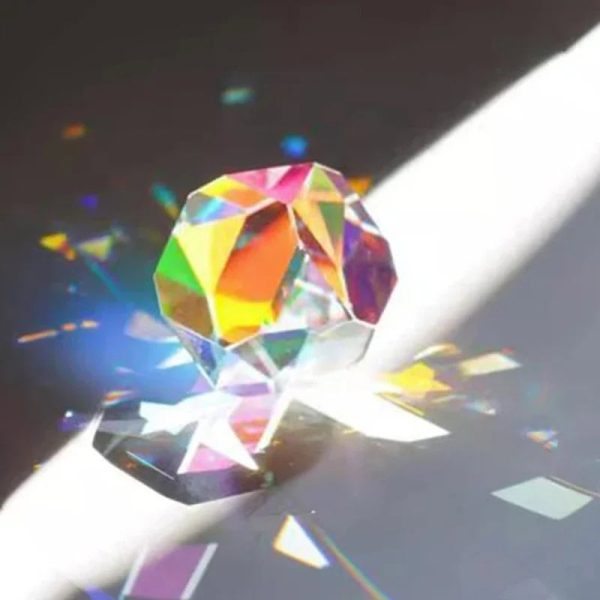Funkelnder Kristall, der Licht in Regenbogenfarben bricht, auf einer weißen Oberfläche mit Schatten und Lichtreflexen.