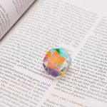 Farbiger, geometrischer Kristall aus Glas auf einem offenen Buch, detailreich und leuchtend, ideal für wissenschaftliche Dekorationen und Sammlerstücke.
