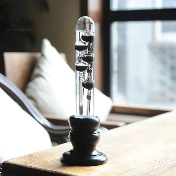Pendel mit schwarzen Kugeln aus Glas, schwingend an einer dünnen Schnur, auf einer Holzoberfläche in einem modernen Raum.