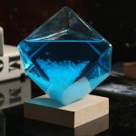 Transparentes, quadratisches Chemie-Reagenzglas mit blauer Flüssigkeit, auf Holzblock präsentiert, wissenschaftliches Dekor.