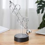 Modernes Pendelspiel aus Metall mit Kugel, ideal für wissenschaftliche Dekorationen und als Lernspielzeug, auf schwarzem Sockel präsentiert.