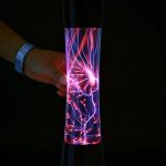 Hand hält eine Plasma-Kugel, die leuchtende elektrische Entladungen zeigt, in einem dunklen Raum.