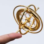 Goldene Atommodell-Skulptur, die auf einem Finger balanciert wird, symbolisiert wissenschaftliche Entdeckung und Innovation. Perfekt für Dekorationen im wissenschaftlichen Stil.